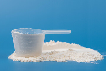 White protein powder, collagen supplement, or baby formula in measuring scoop on blue background. Concept of health, wellness, child food nutrition, fitness, skincare, and childcare. 