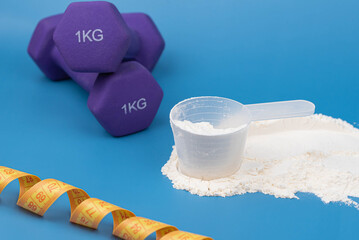 Protein powder in a measuring scoop, with dumbbell and measuring tape on blue background. Fitness goals, muscle building, healthy nutrition, weight loss, balanced diet and active lifestyle.