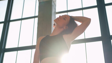 Body warm-up. Neck stretching. Athletic woman in activewear side tilt head with hands training spine muscle in light fitness studio interior.