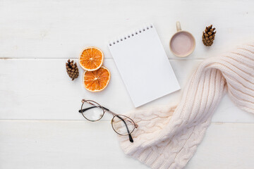 Workspase with notebook, glasses, cozy scarf and cup of coffee with milk on white wooden background. Autumn creative composirion flat lay. Work, online education, goals to do list, home office concept