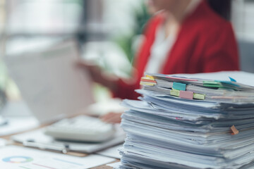 Overwhelmed: A businesswoman's desk is buried under a massive stack of paperwork, symbolizing the...