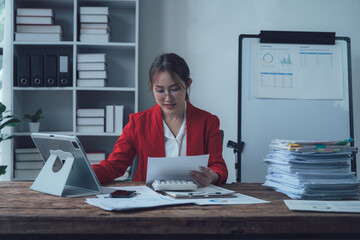 Focused and Determined: A professional woman in a red blazer is engrossed in her work, reviewing...