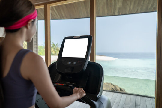 Woman is working out in gym. Doing cardio training on treadmill with white screen mockup , large windows with ocean view raining outside.