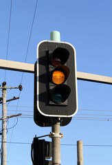 Yellow amber orange light on a set of traffic lights against a blue sky background