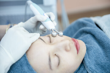 Naklejka premium Beautician hand making ultrasound facial procedure by special equipment.