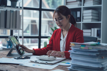 Focused Businesswoman at Desk: A driven businesswoman in a red blazer meticulously works on...