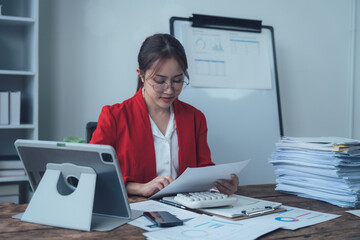 Focused & Determined: A professional woman in a red blazer, meticulously reviewing documents at her...