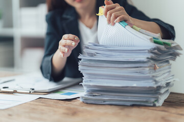 Overwhelmed with Paperwork: A woman sits at her desk, hands buried in a towering stack of...