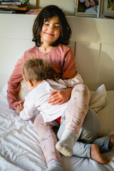 elder sister playing with smaller sitting on the bed at home