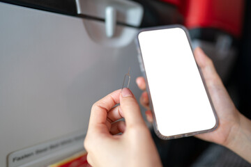 Hand with white blank mobile phone screen mockup with ejector sim card, airplane window background.