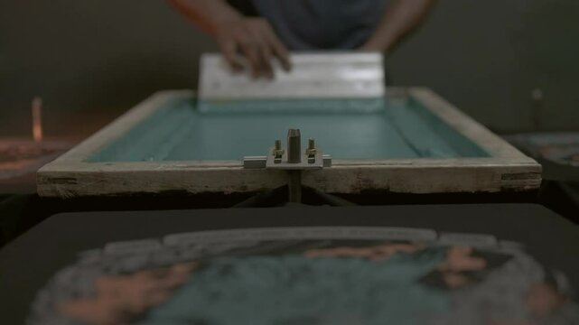 textile factory process, man pushing squeegee inside a printing frame, textile and cloths printing process