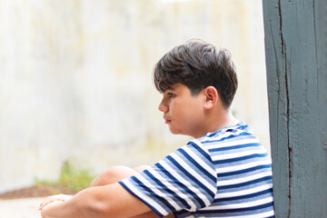 Schoolboy sat with his knees bent against the white wall of the room with a sad expression on his...