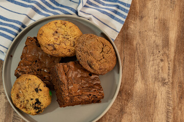 Plate with assorted cookies and brownies on a rustic wood surface with a striped cloth, ideal for dessert or snack concepts.