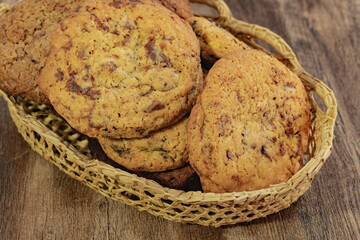 Close-up of assorted chocolate chip cookies in a woven basket on a rustic wooden table.