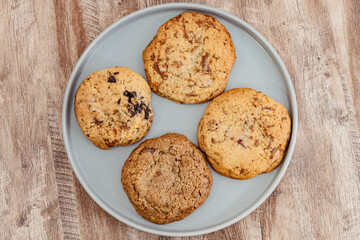 Four chocolate chip cookies on a gray plate on a wooden table, viewed from above, perfect for dessert concepts.