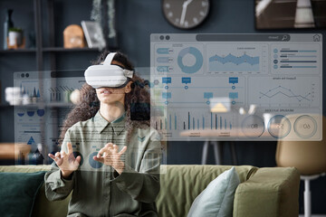 Young woman wearing VR headset sitting on sofa in living room using virtual app, copy space