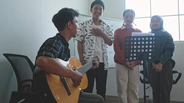 Dolly Shot Of Asian Male Student Playing Guitar To Accompanying His Friends Who Singing In Choir At School