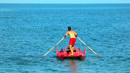 lifeguard on lifeboat rowing in the sea to save swimmers