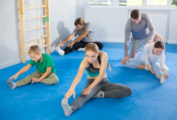 Teen girl, boy, woman and man at group training sitting on floor and stretching muscles under guidance of coach