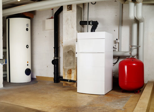 Heating system and hot water tank in residential building. Steel water heater and oil condensing boiler with expansion vessel in boiler room or basement. Lucerne, Switzerland. Selective focus.