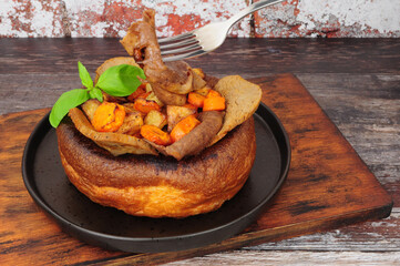 Roast beef slices in a Yorkshire pudding meal with roasted potatoes and carrots on a wooden serving board