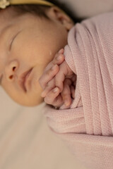 A swaddled baby stands with a little teddy bear. They are wrapped with pink cloth and pink flower headband