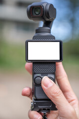 Hand holding pocket camera with white mockup blank screen.