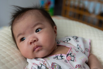 Happy Smiling face Asian Chinese baby girl during lying on bed. Happy Newborn child relaxing in bed