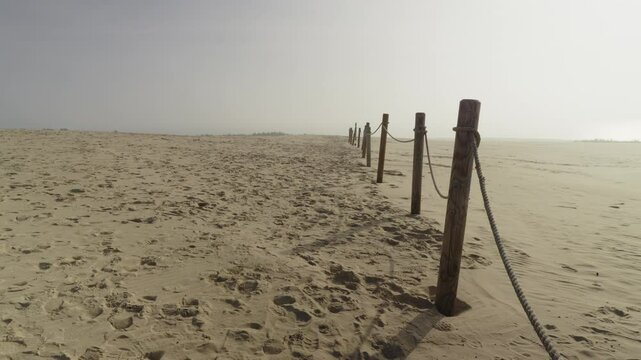 A row of wooden poles connected by a rope in the Polish desert dune of Lacka in Slowinski Park