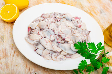 Plate of raw squids surrounded by parsley, lemons, garlic, and olive oil, showcasing fresh...