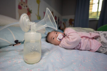 Asian Chinese mother using breast pump machine to pumping milk for her baby in bedroom. Colostrum milk, Transitional milk, Breast Pumping milk concept.