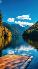 Obraz premium A serene lake scene with a wooden dock surrounded by lush mountains under a bright blue sky with fluffy clouds reflecting on the water.