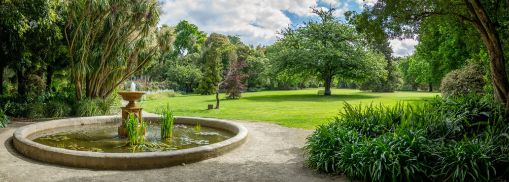Panoramic garden view with a circular fountain in an ornamental pond, lush landscaping, and a manicured lawn. A beautiful park with a water feature and various trees.Colac Botanic Gardens, Australia