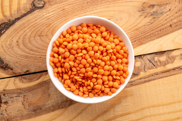 Raw red lentils in a ceramic dish on a wooden table, macro, top view.