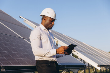 African American Engineer Inspecting Solar Panels With Digital Tablet Outdoors