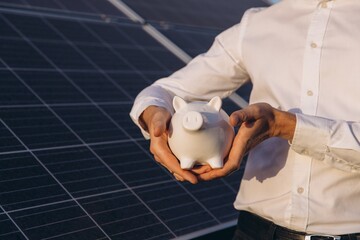 Man Holding Piggy Bank in Front of Solar Panels