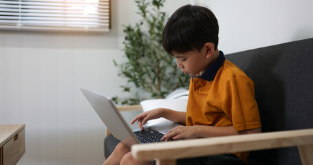 little schoolboy boy does homework on laptop at home. distance learning concept
