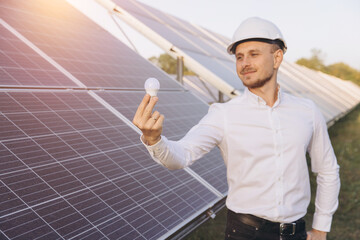 Engineer Holding LED Bulb in Front of Solar Panels