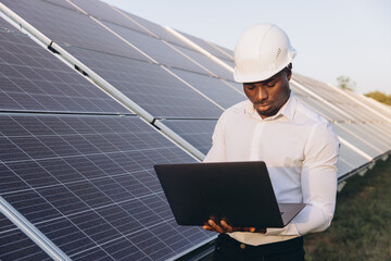 African American Engineer Working on Laptop Near Solar Panels at Solar Farm