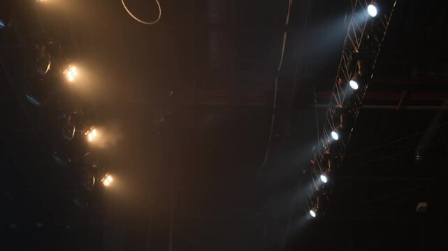 A row of spotlights mounted on a truss on the ceiling of the filming studio shine yellow light on the stage and on the auditorium
