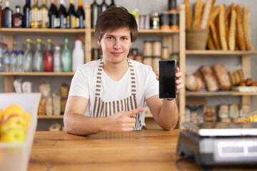 Man employee of shop store offers to download and install mobile application on phone. Stores website, applications, online purchases and reservations of fresh products in app