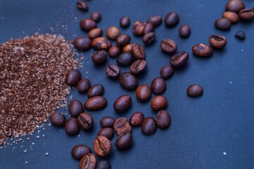Instant coffee powder that has been mixed with granulated sugar, and coffee beans scattered around it on a dark background. With a close look.