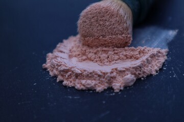Loose powder and makeup brush, applying powder on face on black background. Concept of cosmetics, cosmetology. Close up view.
