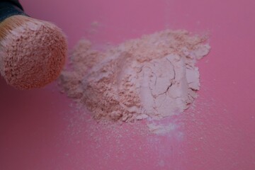 Loose powder and makeup brush, applying powder on face on pink background. Concept of cosmetics, cosmetology. Close up view.
