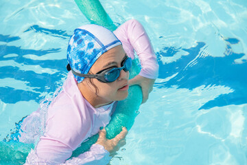 Girl with Down syndrome bathing in the pool on a summer day. inclusion, trisomy 21. wears diving...
