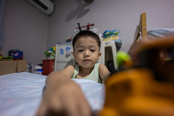 Naklejka premium Cheerful young boy sitting and smiling while playing with a yellow truck at bedroom