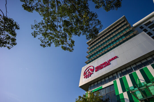 Modern building of AIA insurance Company with green stripes and a tree reaching for the sky on a sunny day