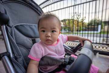 Cute asian baby girl sitting in a stroller and waiting to go out