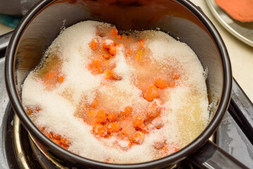 Sea buckthorn berries sprinkled with sugar in a saucepan for making jam.
