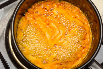 Boiling sea buckthorn berries with sugar in a saucepan for making jam.